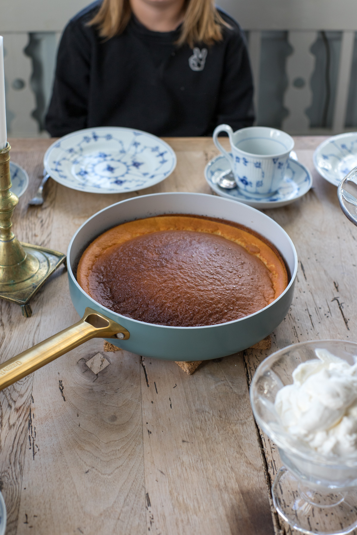 Ganzer Dutch Baby in der Pfanne auf einem Holztisch mit blau-weißem Geschirr und einer Schale Sahne
