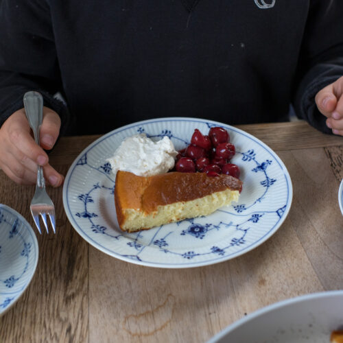 Ein Stück Dutch Baby mit Kirschen und Sahne auf einem blau-weiß gemusterten Teller