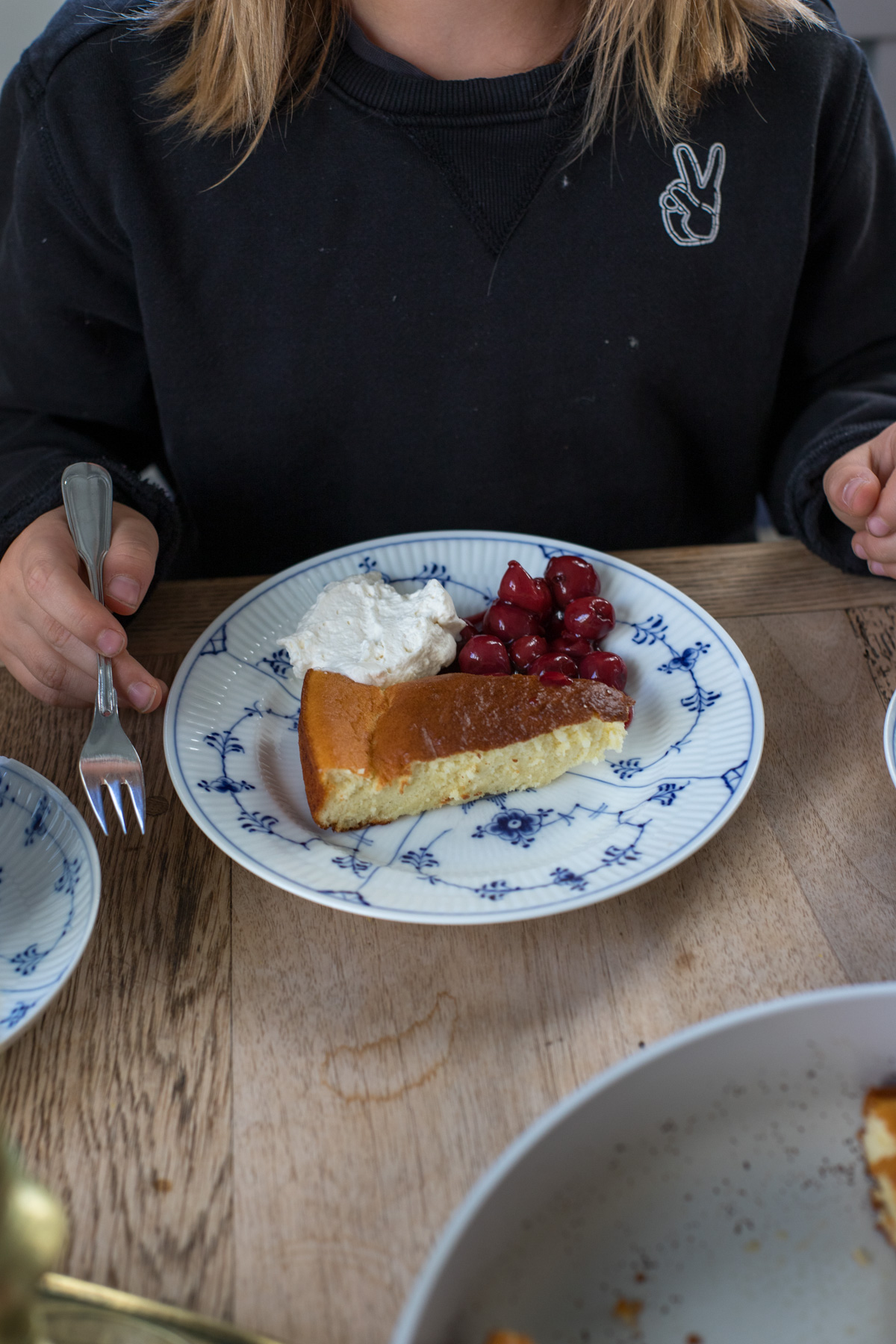 Ein Stück Dutch Baby mit Kirschen und Sahne auf einem blau-weiß gemusterten Teller