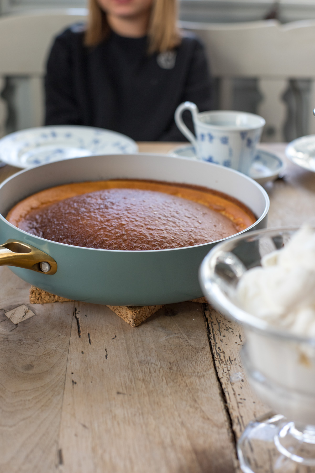 Goldbraun gebackener Dutch Baby in einer hellen Pfanne mit goldenem Griff auf einem gedeckten Holztisch