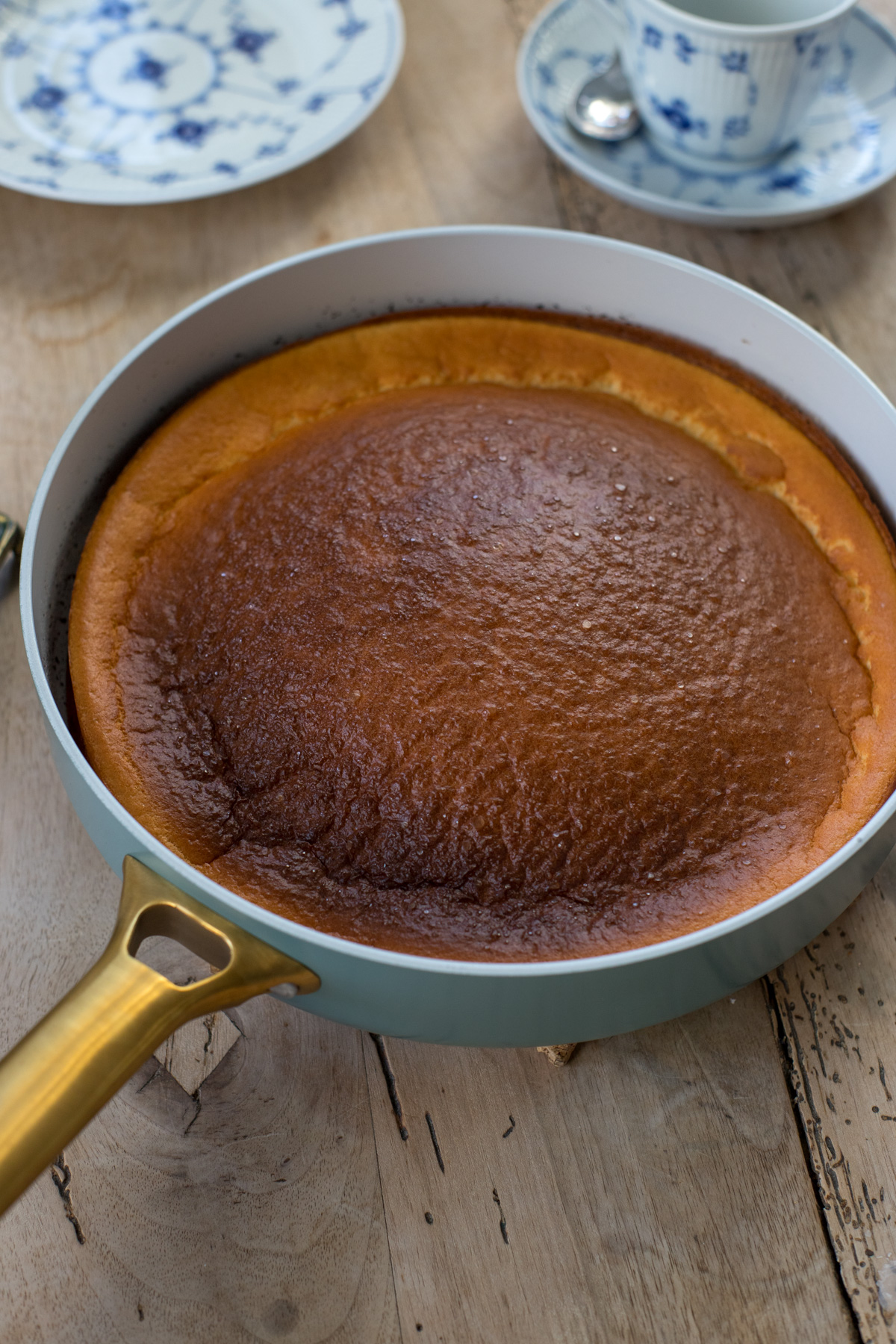 Dutch Baby mit goldbrauner Oberfläche in einer hellen Pfanne, schräg von oben fotografiert